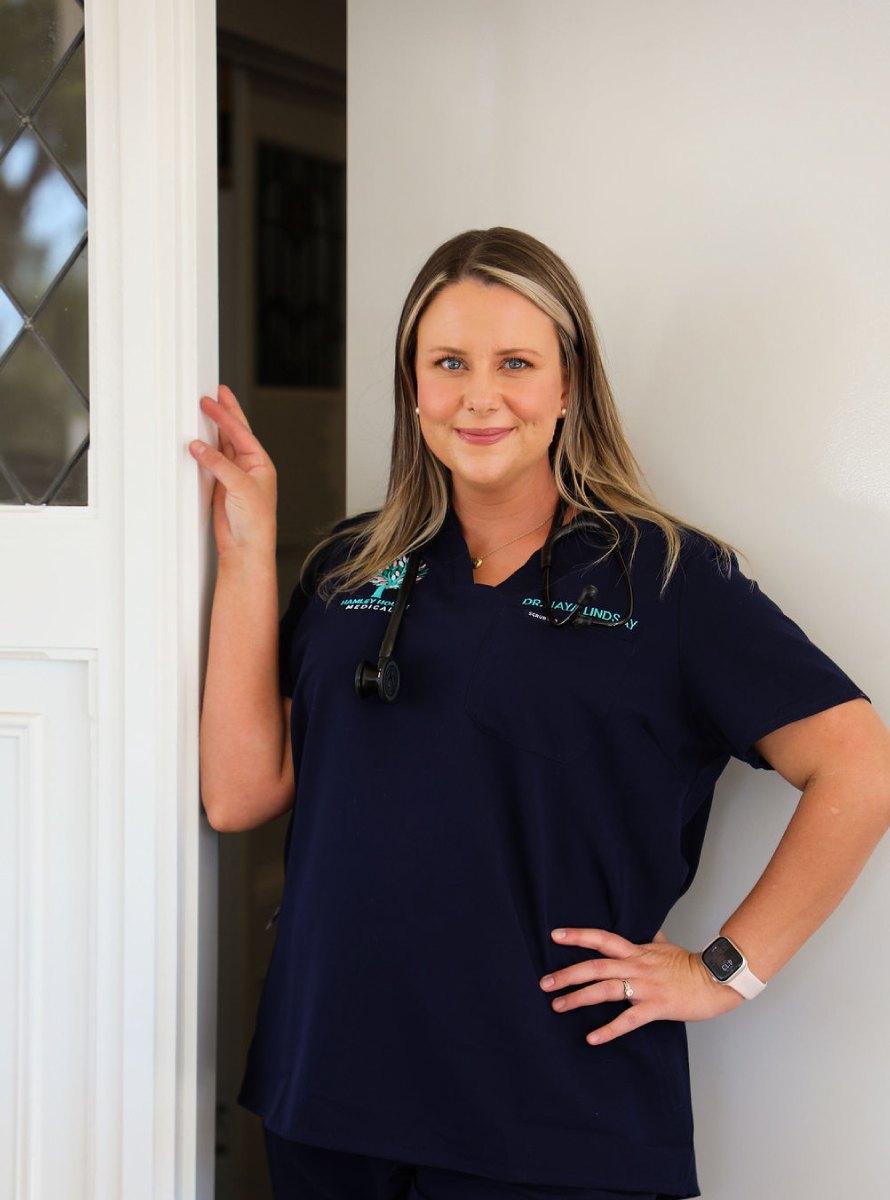 Dr Jaya Lindsay leaning in a white doorway, smiling